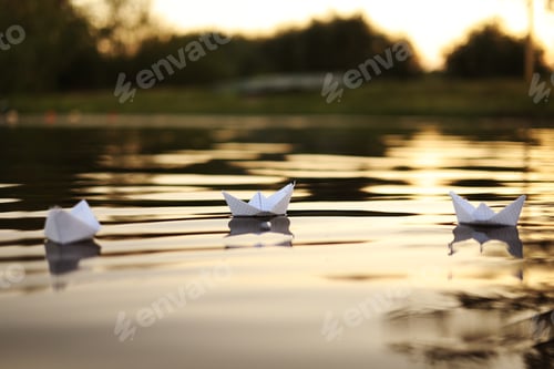 Preview: three paper boats floating on the waves in the water at a beautiful sunset. homemade Origami boats