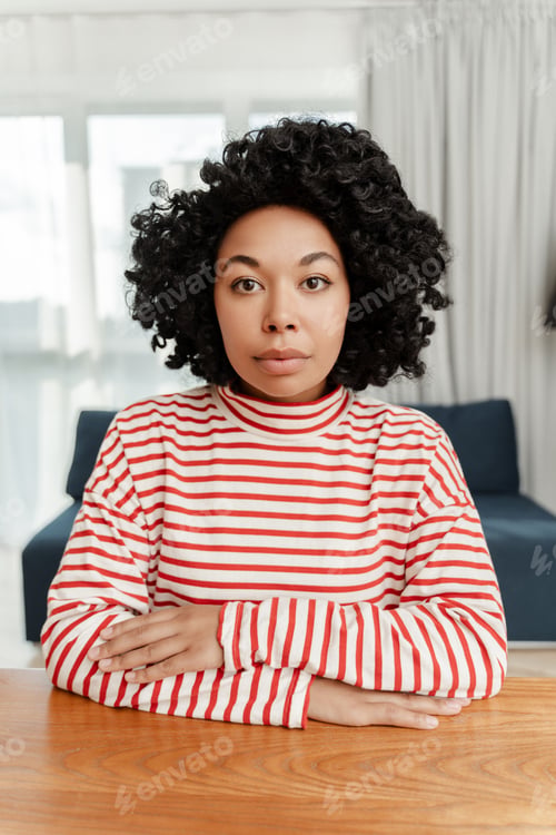 Preview: Portrait of serious pensive curly African American woman sitting at desk looking at camera