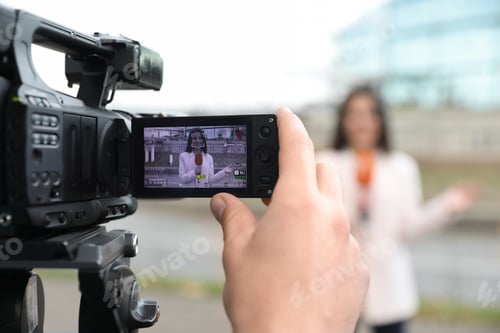 Preview: Young male journalist and video operator working on city street, focus on camera display