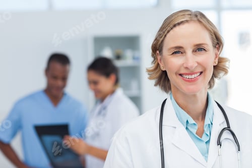 Preview: Woman Doctor Smiling And Looking To The Camera While A Medical Team Is Working