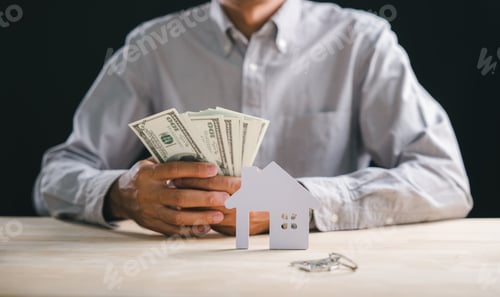 Preview: Property purchase concept shows hands holding dollars, keys beside paper house model representing