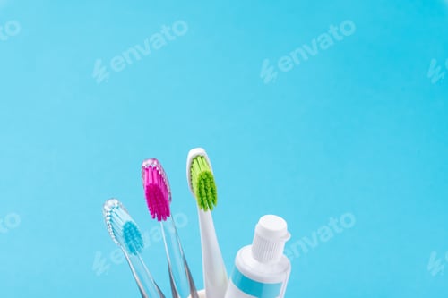 Preview: Three plastic colorful toothbrushes in glass on a blue background, close up
