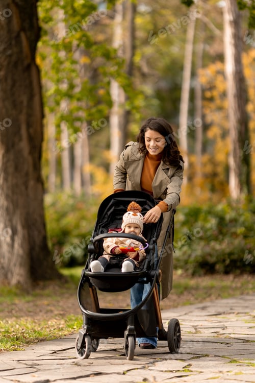 Preview: Young woman with cute baby girl in baby stroller at the autumn park