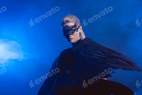 Preview: beautiful mysterious woman with lace mask and black angel wings on dark blue background with copy