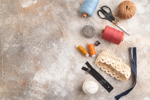 Preview: Sewing accessories: scissors, thread, thimbles, braid on brown concrete background. Top view, flat l