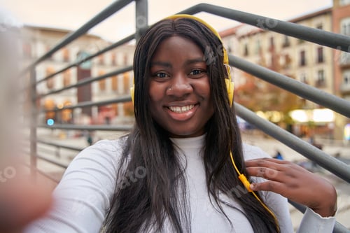 Preview: African-American woman with yellow headphones taking a selfie with a cell phone