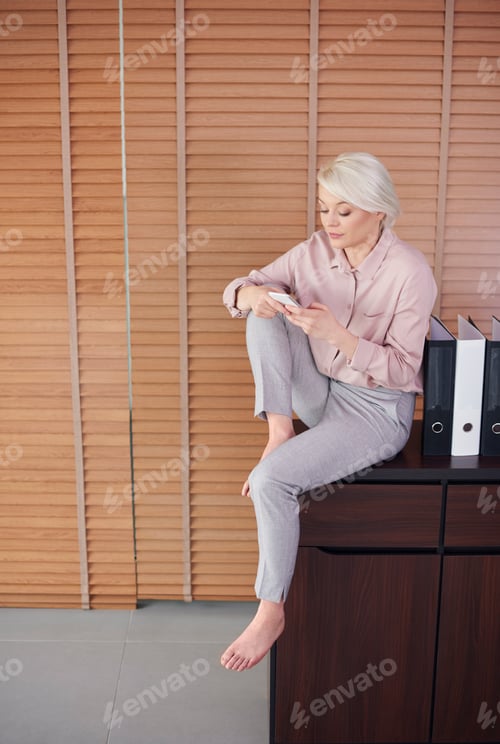 Preview: Barefoot woman sitting on drawer and texting