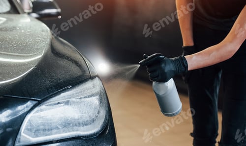 Preview: Spraying the vehicle. Modern black automobile get cleaned by woman inside of car wash station
