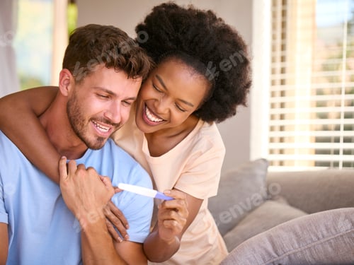 Preview: Excited Multi-Racial Couple In Bedroom At Home Celebrating Positive Pregnancy Test Result
