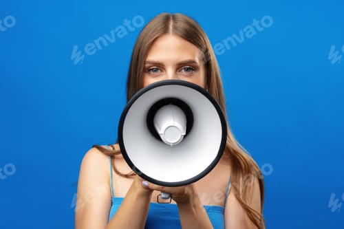 Preview: Young pretty woman with a megaphone against blue background in studio