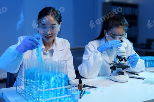 Preview: Two female scientists wearing lab coats and safety glasses are conducting research in a laboratory,