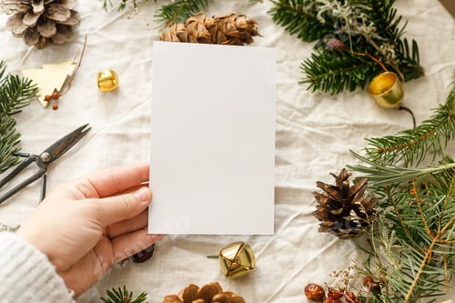 Preview: Christmas card mock up. Hand holding empty greeting card on rustic table with fir branches
