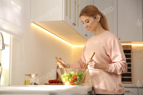 Preview: Young woman cooking salad at counter in kitchen