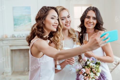 Preview: beautiful bride with bridesmaids taking selfie before ceremony