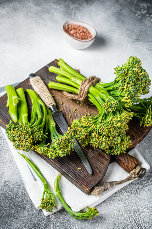 Preview: Fresh bunch of Broccolini sprouts on cutting board ready for cookining. White background. Top view