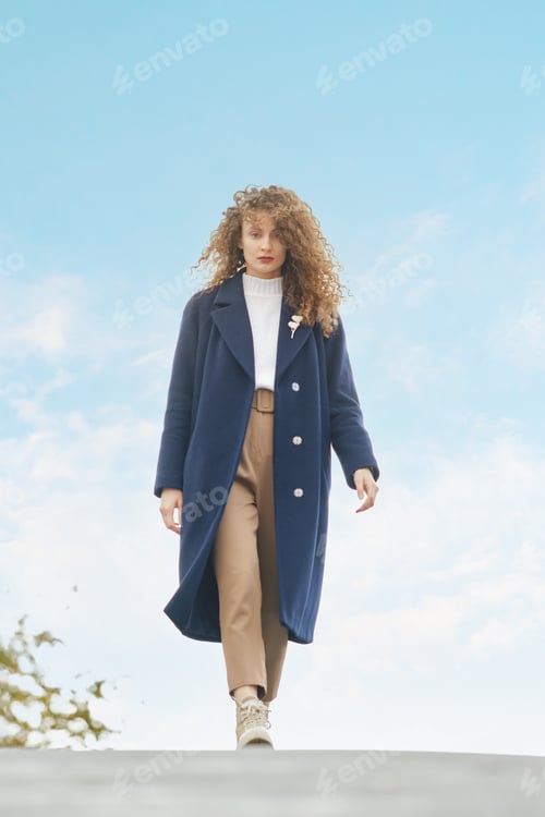 Preview: Stylish woman in wool coat walks on the bridge in sunny day