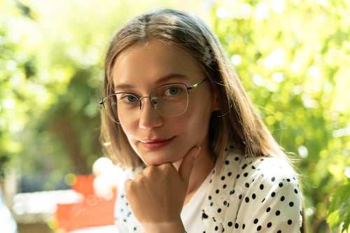 Preview: Portrait of confident young woman wearing glasses in green outdoor setting