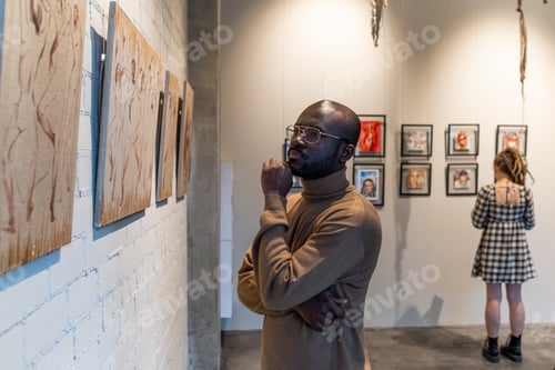 Preview: Serious African man in brown pullover looking at painting