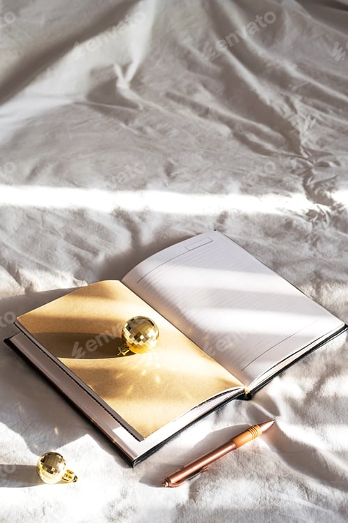 Preview: Open notebook, pen, sparkling Christmas balls on bed. New year goals. Cozy festive holiday at home.