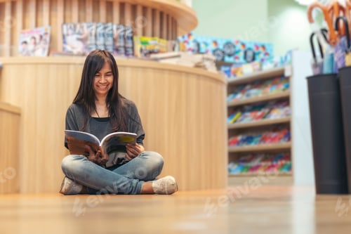 Preview: Asian woman holding book reading at bookshelf in university library.