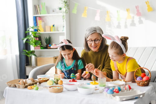 Preview: Smiling grandmother and granddaughters painting easter eggs together at home