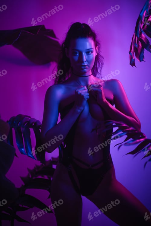 Preview: Sexy Lingerie Model in Neon Led Light in Studio Among Tropical Foliage