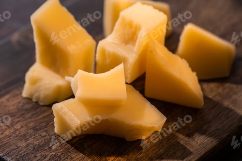 Preview: close up view of wooden platter with Grana Padano cheese on weathered surface in sunlight