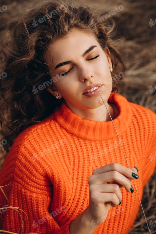 Preview: young curly girl in an orange sweater against the backdrop of autumn nature
