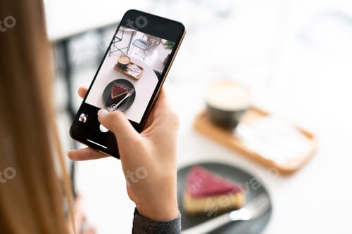 Preview: Cappuccino and tiramisu cake on touchscreen of smartphone held by young woman