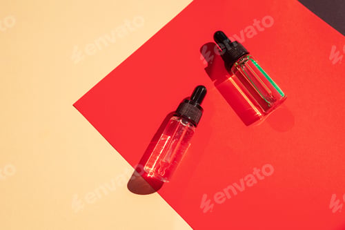 Preview: Two glass bottles with cosmetic liquid on bright red background with shadows and light reflections.