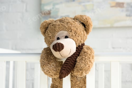 Preview: close up view of teddy bear hanging on white wooden baby crib in room