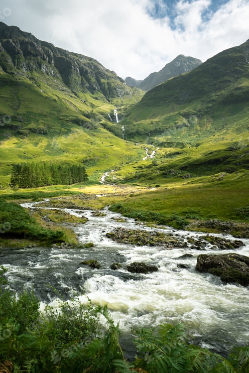 Preview: Vertical shot of a river surrounded by the mountains and meadows in Scotland