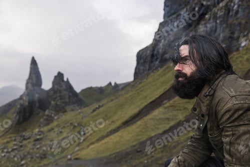 Preview: A man on a slope with a backdrop of rock pinnacles on the skyline, a dramatic windswept landscape.