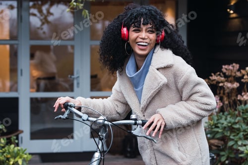 Preview: Cheerful black woman in headphones with bicycle