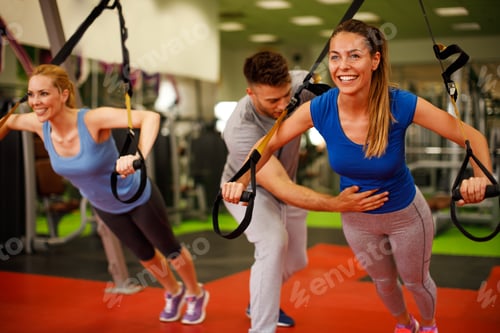 Preview: Personal trainer assisting young woman while exercising with trx in the gym