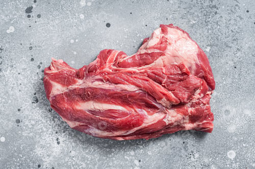 Vista previa: Boneless Raw lamb neck meat on a butcher table. Gray background. Top view