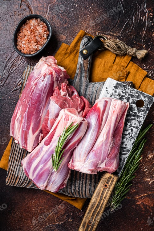 Preview: Uncooked Raw lamb mutton shanks on a butcher board. Dark background. Top view