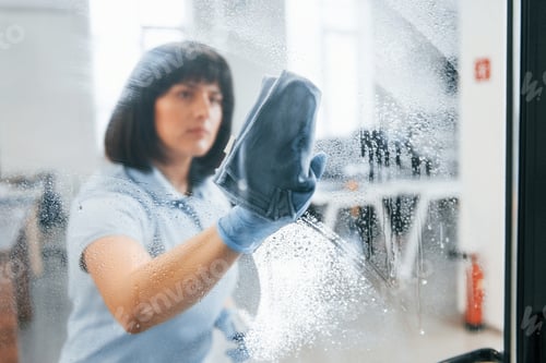 Preview: Woman cleaning dirty window by using towel. View through the glass