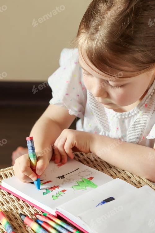 Preview: Little girl 6 years old draws with wax crayons in a sketch book