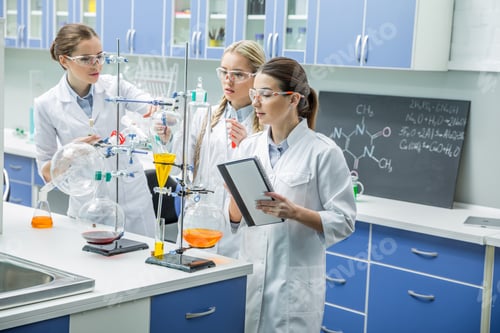 Preview: Three female scientists in protective goggles making experiment in chemical laboratory