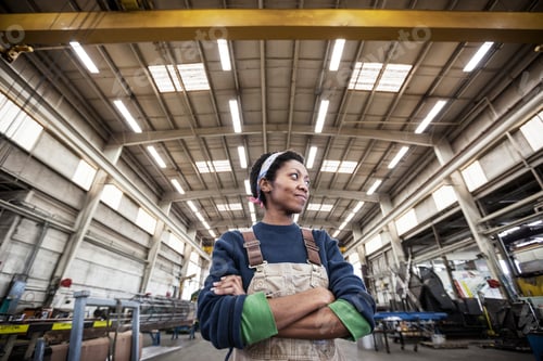 Preview: Black woman factory worker wearing coveralls in a large sheet metal factory.