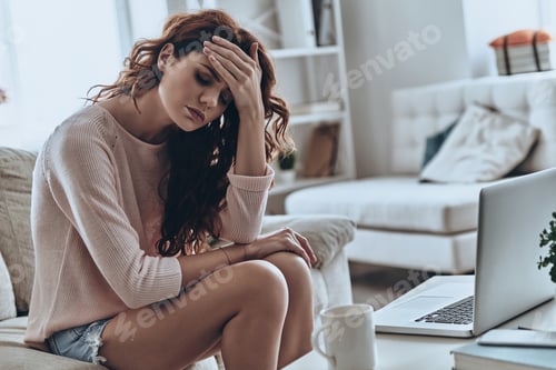 Preview: In a bad condition. Sick young women suffering from headache while sitting on the sofa at home
