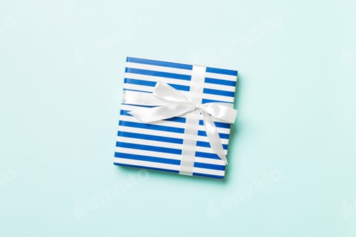 Preview: Gift box with white bow for Christmas or New Year day on blue background, top view with copy space