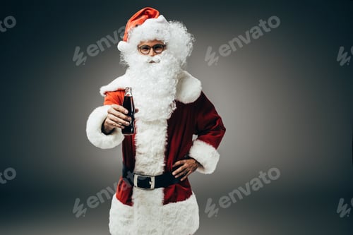 Preview: smiling santa claus in costume standing with cream soda bottle isolated on grey background