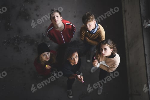 Preview: Top view of group of teenagers gang standing indoors in abandoned building, looking at camera.