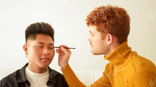 Preview: Concentrated gay man applying make up to her partner
