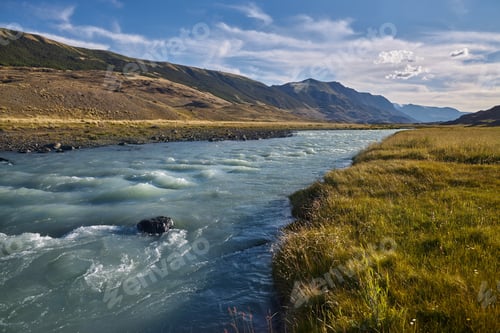 Preview: Flowing river in a valley with mountains and grassy banks at midday