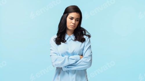 Preview: displeased young woman in shirt standing with crossed arms isolated on blue