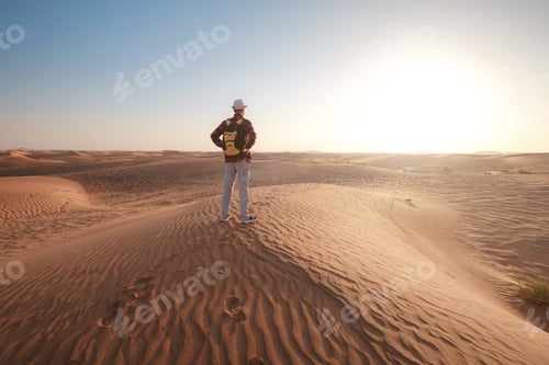 Preview: Desert adventure. Young man with backpack walking on sand dune. Dubai, United Arab Emirates
