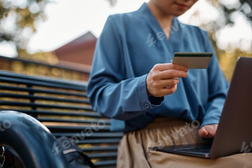 Preview: Close up of woman e-banking with credit card and laptop outdoors.